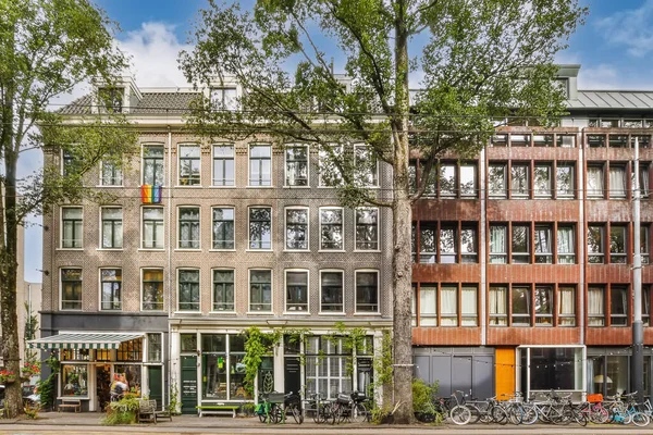 stock image an apartment building in amsterdam, with bicycles parked on the sidewalk and trees lining the street behind it - stock photo