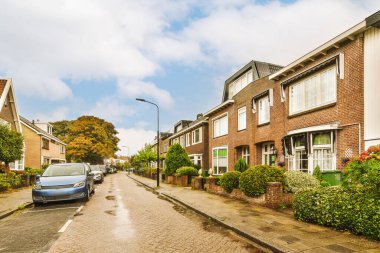 Arabaların park ettiği bir cadde ve evlerinin arkasına tuğlalar örülmüş evler.