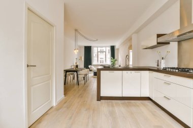 Ahşap döşemeli, beyaz dolaplı ve tezgahlı bir evde mutfak ve yemek odası.