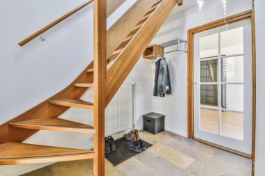 Beyaz duvarları ve ahşap merdivenleri olan bir odada ikinci kata çıkan ahşap bir merdiven duvarda bir ayna var.