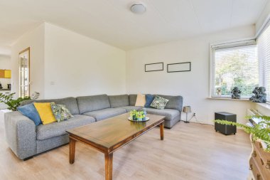 Güneşli bir günde pencerenin önünde kanepesi ve sehpası olan bir oturma odası bahçeye bakıyor.