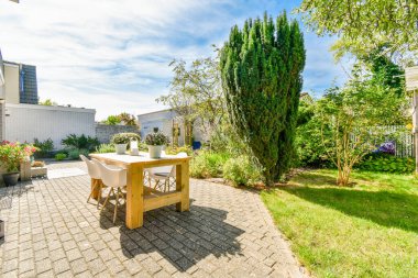 Bahçenin her iki tarafında yeşil ağaçlarla çevrili, ortasında bir masa ve sandalyeler olan bir arka bahçe.