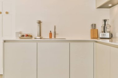 Lavabonun önündeki tezgahın üstünde beyaz dolapları ve aletleri olan bir mutfak açık bir kapıdır.