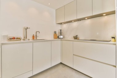 Fotoğrafın ortasında beyaz dolapları ve tezgahı olan bir mutfak ön pencereden çekiliyor.