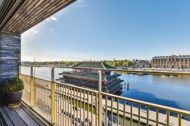 Güneşli bir günde nehirden geçen bir tekne mavi gökyüzü ve beyaz bulutlar bir balkondan çekiliyor.