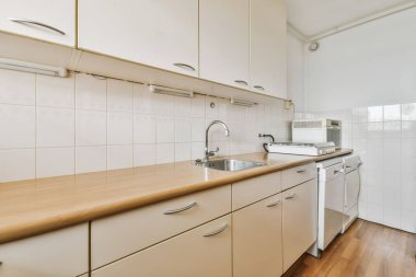 Arka duvarında ahşap tezgah ve beyaz dolaplar olan bir mutfak. Lavabonun yanında bulaşık makinesi var.