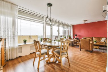 Odanın ortasında kırmızı duvarları ve ahşap döşemeleri olan bir oturma odası, dört kişilik bir yemek masası var.