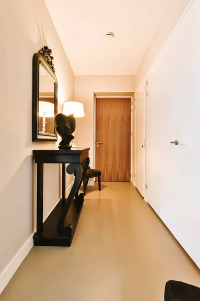 a hallway with a mirror on the wall and a black chair in the corner next to the door, there is a lamp