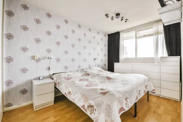 a bedroom with floral wallpaper on the walls and wood flooring in front of the bed, there is a window to the