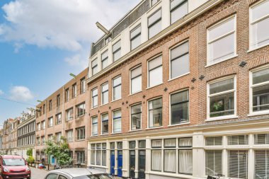 Kenarında arabaları olan bir şehir caddesi ve fotoğrafın ortasındaki binalar açık mavi gökyüzü.