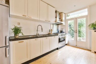 Lavabonun önündeki adada beyaz dolapları ve siyah tezgahları olan bir mutfak açık bir kapıdır.