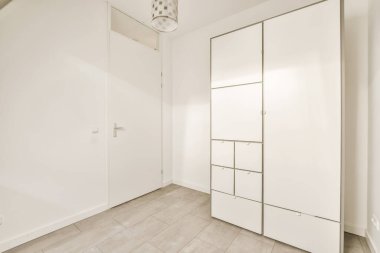 Beyaz duvarları ve ahşap döşemeleri olan boş bir oda. Köşedeki duvarda bir ayna var.