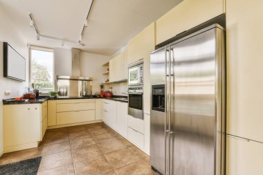 Bu fotoğraftaki tezgahlarda beyaz dolaplar ve paslanmaz çelik aletlerle modern bir mutfak var.