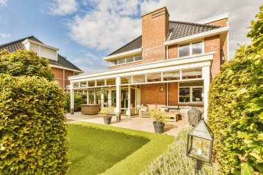 Hollanda 'da bahçeli bir ev ve güneşli bir günde çalılar ve çalılarla çevrili yeşil çimenler.