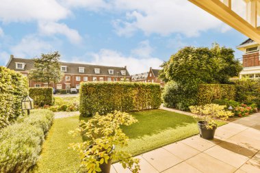 Ön tarafında çiçekler ve bitkiler olan bir dış alan. Görüntü içeriden alınıyor ama kimse görünmüyor.