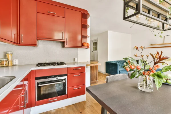 a kitchen with red cabinets and white counter tops in the center of the photo is taken from the living room to the dining area