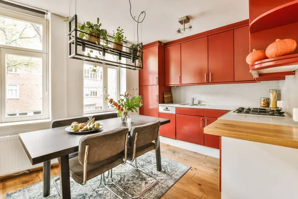 a kitchen and dining area with red cabinets, white counter tops and wooden flooring in an apartment living room