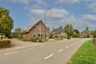 Arka planda evler ve her iki tarafında ağaçlar olan boş bir yol boyunca park yerine giden bir cadde.