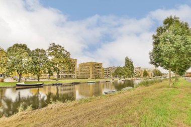 Arka planda ağaçlar ve kıyı boyunca park etmiş tekneler olan bir su kütlesinin kenarındaki bazı binalar.