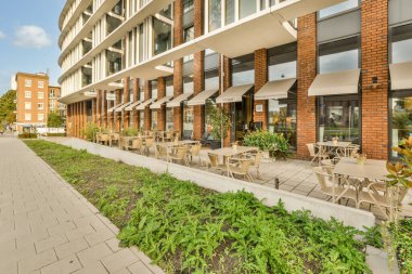 Bir binanın önündeki kaldırımda masa, sandalye ve şemsiyelerle dolu bir alan.