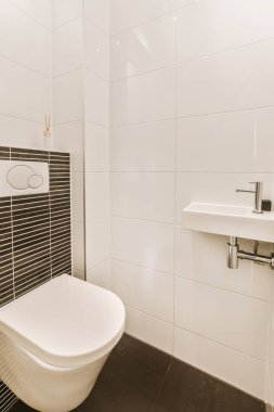Duvarlarında siyah beyaz fayanslar olan modern bir banyo. Tuvalet ve lavabo temiz ve kullanıma hazır.