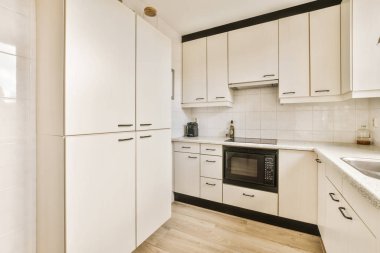 Tezgahın etrafında beyaz dolaplar ve siyah süslemeler olan bir mutfak.