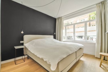 Siyah duvarları ve beyaz yatağı olan bir yatak odası, ahşap döşeme ve büyük pencereler parlak.