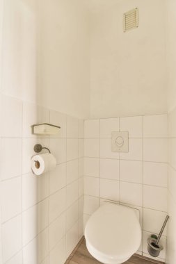 Duvarları ahşap döşemeli ve fayanslı küçük bir banyoda beyaz bir tuvalet görülebilir.