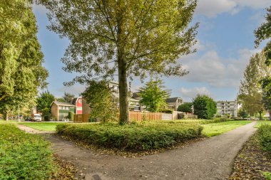 Yerleşim alanının ortasında, yerde yaprakları ve sağda evleri olan bir ağaç.