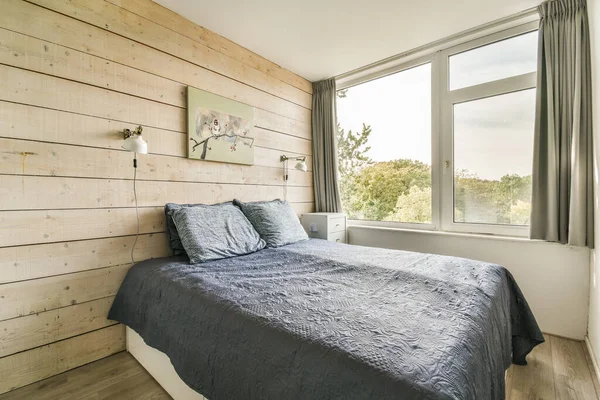 a bed in a room with wood paneling on the wall behind it and a window that looks out onto trees