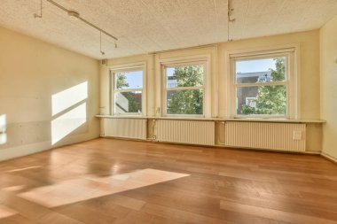 Ahşap döşemeli boş bir oda ve apartmanın önündeki sokağa bakan iki pencere.