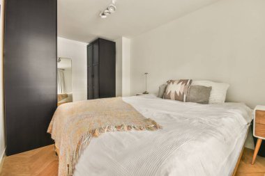 Yatağı, şifoniyeri ve aynası olan yatak odası yatağın önünde beyaz ve siyahtır.