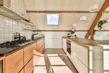 Lavabonun önündeki adada ahşap dolaplı ve siyah tezgahlı bir mutfak pencereden görülüyor.