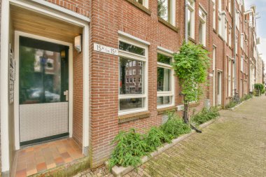 Kapılarında bitkiler büyüyen tuğla bir bina ve binanın yan tarafında 