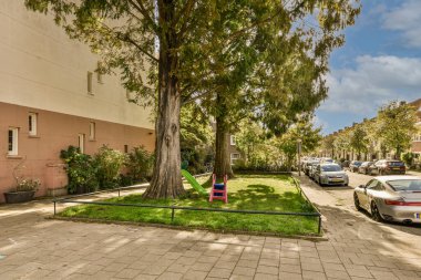 Caddenin ortasında bir ağaç yolun iki yanına park edilmiş arabalar ve yol kenarında ağaçlar var.