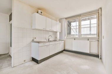 Odanın ortasında beyaz dolapları ve aletleri olan boş bir mutfak. Dışarıya açılan bir pencere var.