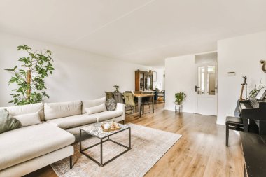 Köşesinde piyano olan bir oturma odası ve sağdaki yemek salonuna açılan açık bir kapı.