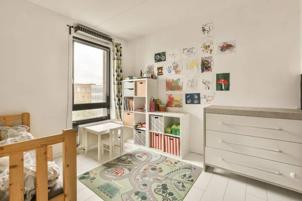 a childs room with a bed, dresser and toy car on the floor in front of the window