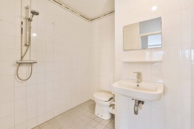 Tuvaleti ve duş başlığını lavabonun üstündeki duvara monte eden beyaz kiremitli bir banyo.