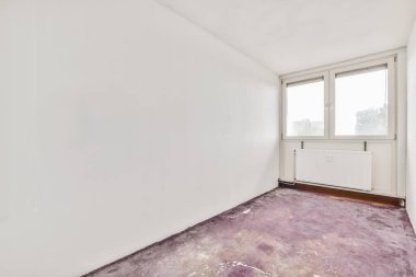 Beyaz duvarları ve mor halıları olan boş bir oda pencerenin önünde sokağa bakıyor.