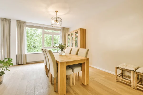 a dining table and chairs in a room with wood floors, white walls and large windows looking out onto the street