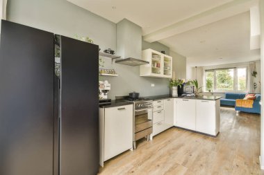 Odanın ortasında ahşap döşemeli ve siyah aletli modern bir mutfak açık bir yaşam alanıdır.