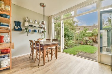 Ahşap zeminli bir yemek odası ve arka bahçedeki verandaya açılan sürgülü cam kapılar.