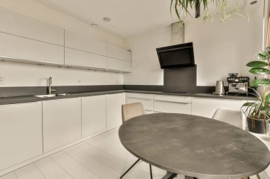 Bu fotoğraftaki tezgahların üzerinde beyaz dolaplar ve siyah tezgahlar olan küçük bir mutfak içeriden çekilmiş.