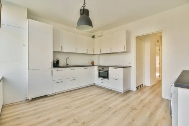 Odanın ortasında beyaz dolapları ve ahşap döşemeleri olan bir mutfak alanı var.