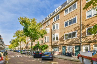 Caddenin her iki tarafında arabaların ve caddenin ortasında binalarla dolu ağaçların olduğu bir şehir caddesi.