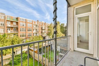 Arka planda ağaçlar ve binalar olan bir balkon, aşağıdaki sokağa bakan bir apartman penceresinden alınmış.