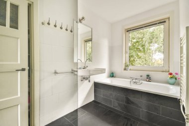 Yerde siyah ve beyaz fayanslı bir banyo, duş kabini ve lavabo içeriden çekilen bu fotoğrafta görülebilir.