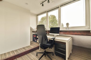 Pencerenin önündeki duvarda masası, sandalyesi ve bilgisayar monitörü olan bir ofis.