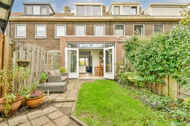 Bahçenin ortasında yeşil çimenler ve bitkiler olan bir arka bahçe, arka kapıya doğru bakıyor